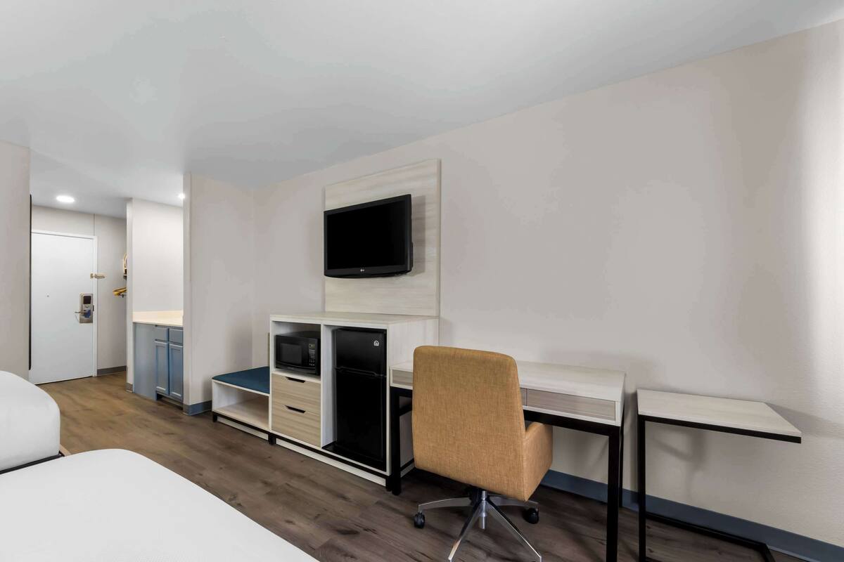 A modern hotel room with a bed, a desk with a computer, a TV, and a microwave.