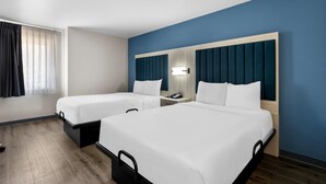 Habitación de hotel con dos camas, una mesita de noche con teléfono, una ventana con cortinas y suelo de madera.
