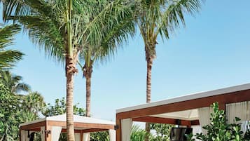 A private garden with a wooden deck, a canopy bed, and palm trees.