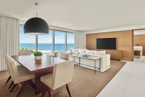 A modern living room with a large dining table, white sofas, and a TV against a wooden wall.