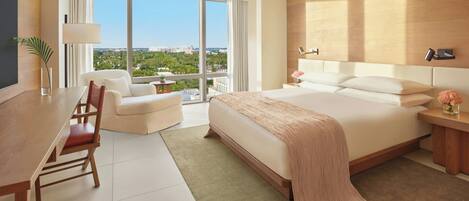 A modern hotel room with a large bed, a desk, a chair, and a view of the city through large windows.