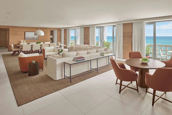 A modern hotel room with a large sofa, dining table, and chairs. There is a view of the ocean through large windows. - The Miami Beach EDITION (Miami Beach)