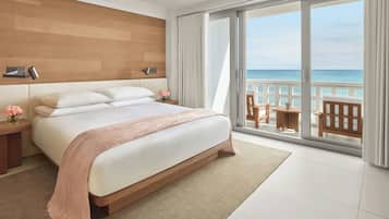 Una habitación de hotel moderna con una cama grande, vista al océano y un balcón con mobiliario exterior.