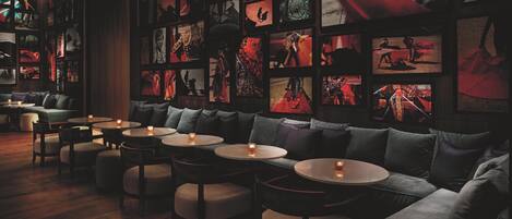 A dimly lit lounge area with a sofa, round tables, and wall-mounted picture frames.