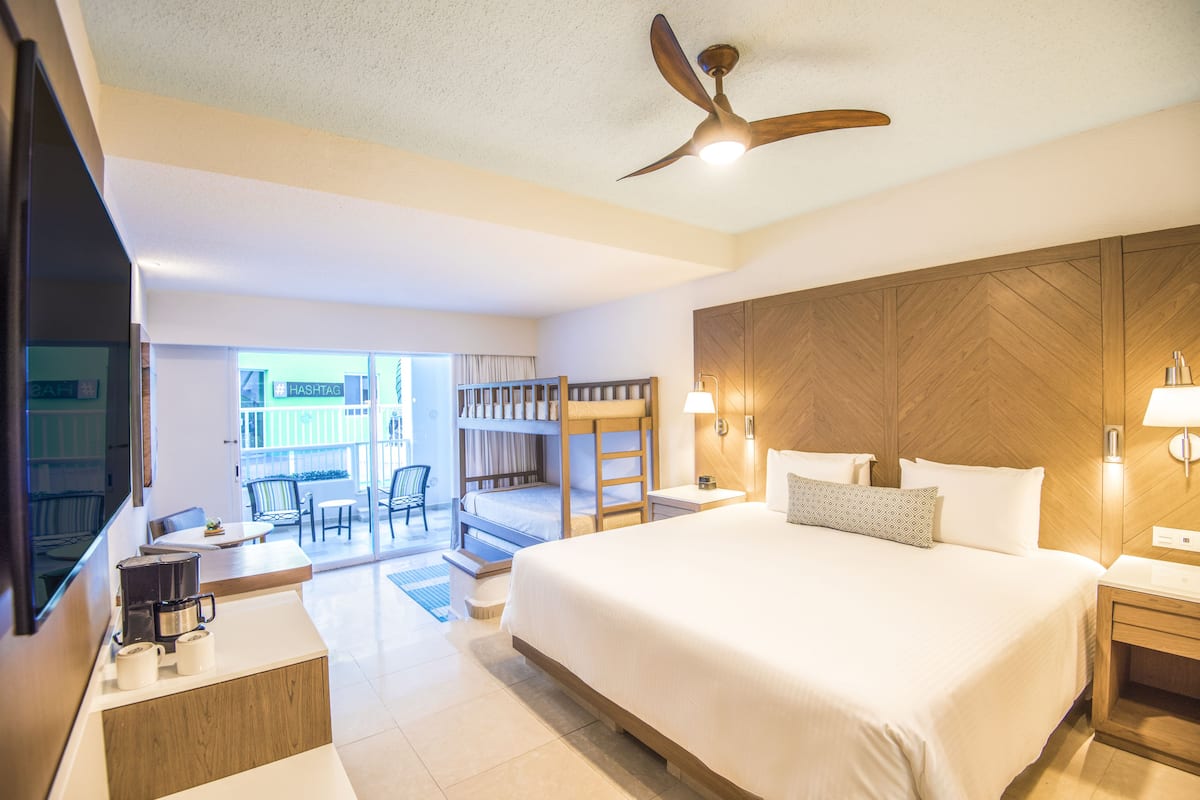 A hotel room with a large bed, a ceiling fan, a TV, a coffee maker, and a view of the outside balcony.
