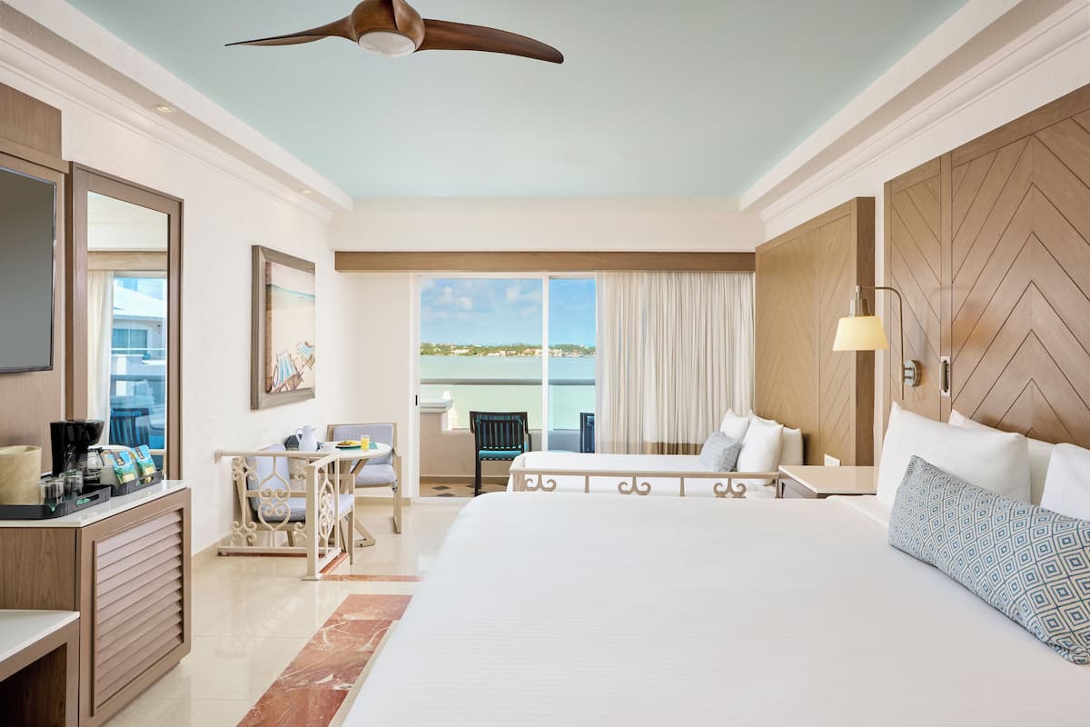 A hotel room with a large bed, a desk, a chair, a large window with curtains, and a ceiling fan.