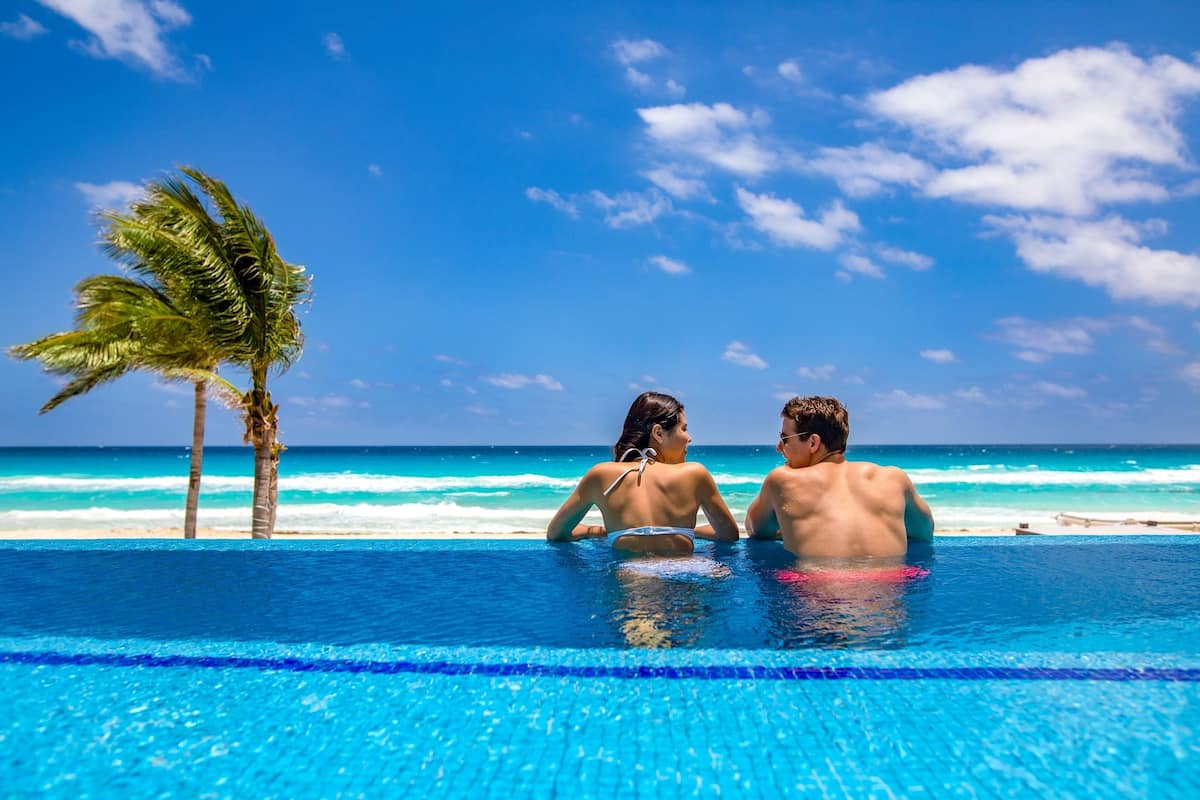 A couple in a swimming pool with a view of the ocean and palm trees.