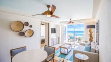 Een ruime woonkamer met een ronde tafel, banken en een plafondventilator. Er zijn decoratieve wandplaten en een uitzicht op de oceaan door grote ramen.