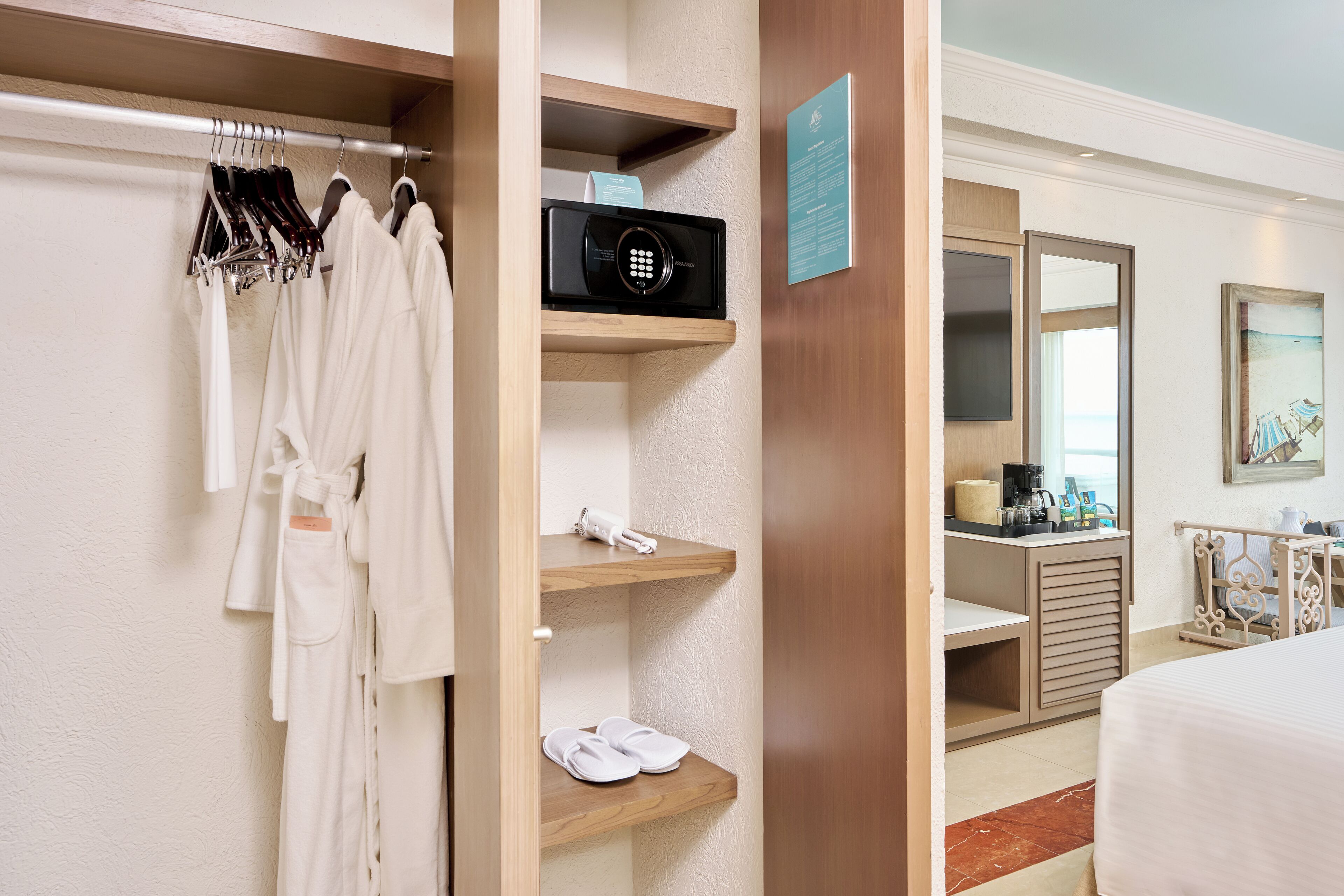 Habitación de hotel con armario de madera, microondas, estante con pantuflas, cafetera y cama.