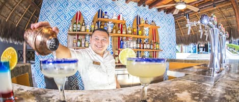 A bar area with a bartender preparing drinks, a patterned wall, and a ceiling fan.