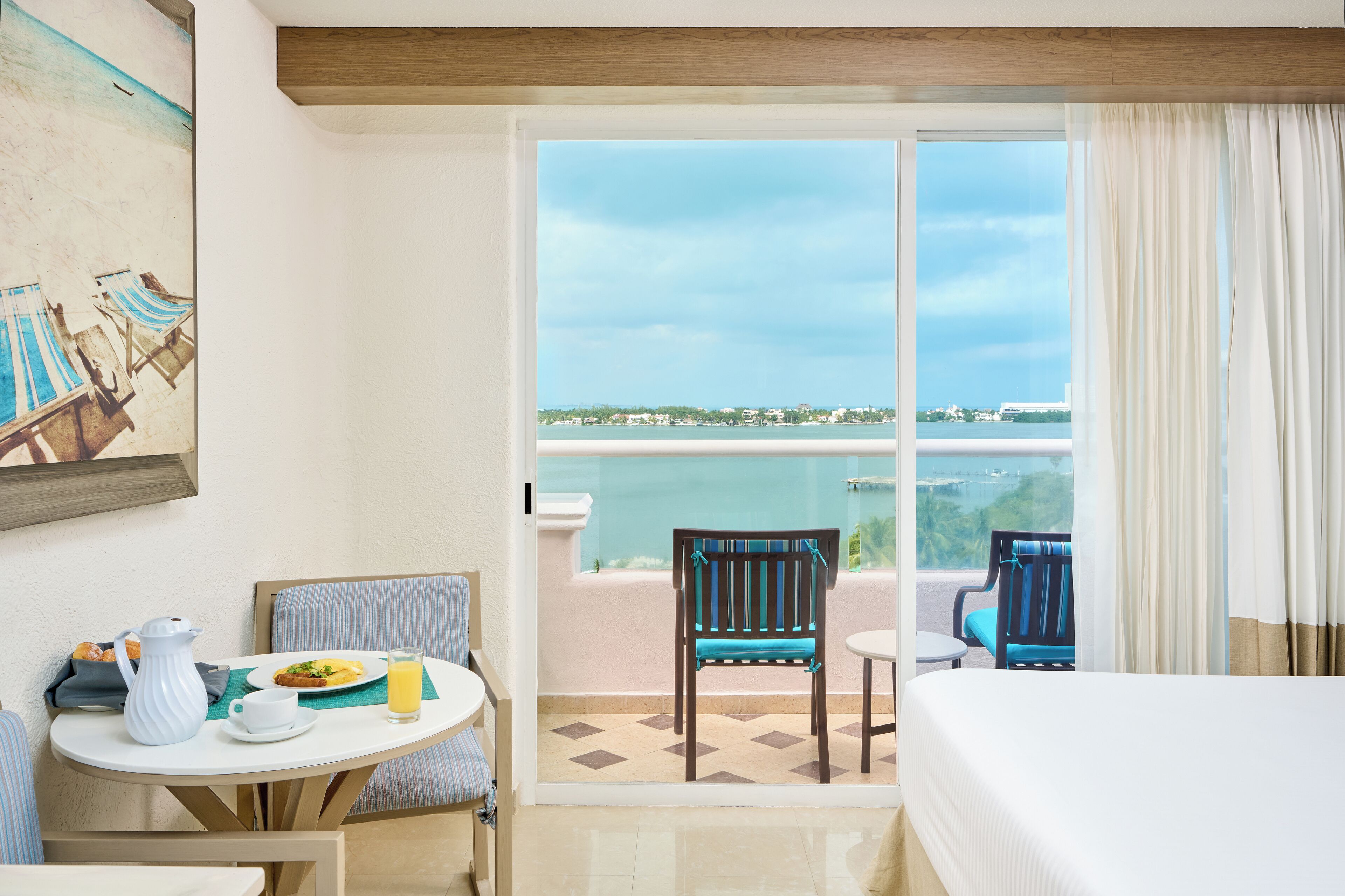 Ein Hotelzimmer mit Balkon, einem Esstisch mit Stühlen, einem Bett und einem Bild an der Wand.