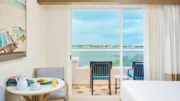 Habitación de hotel con balcón, una mesa de comedor con sillas, una cama y un cuadro en la pared.