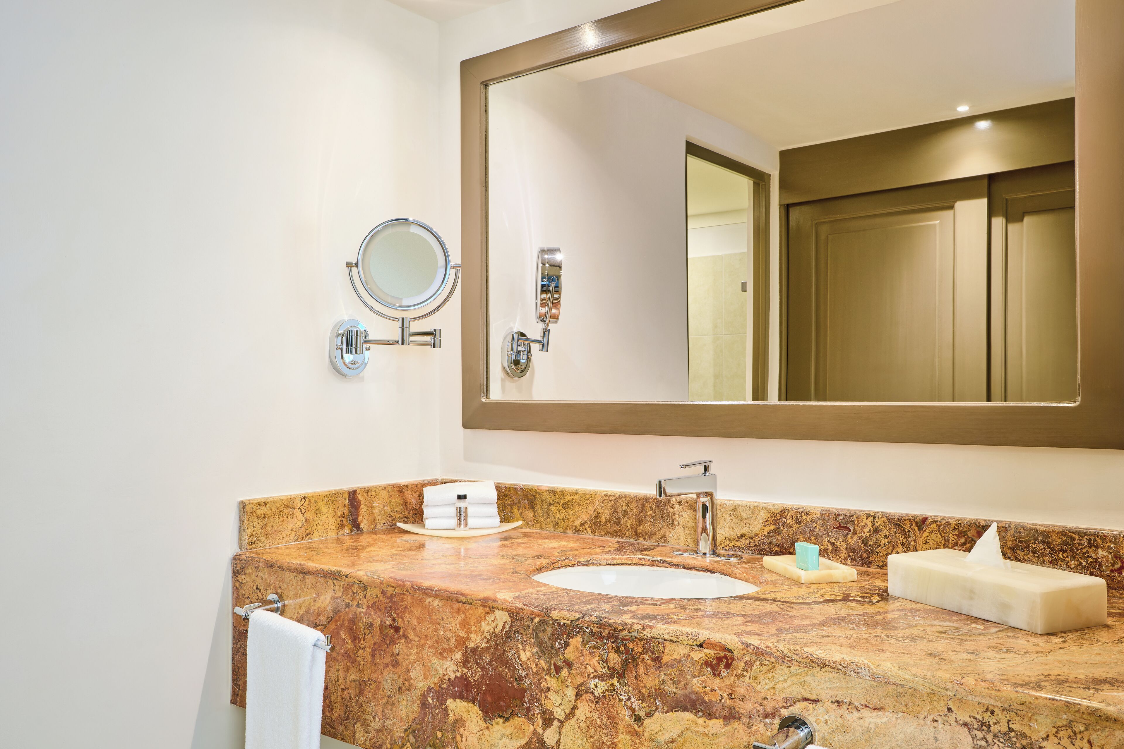 A bathroom with a marble sink, a large mirror, and a towel rack.