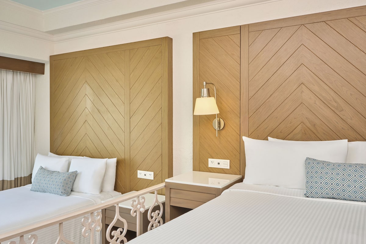 A hotel room with two beds, a nightstand, a lamp, and a wooden headboard.