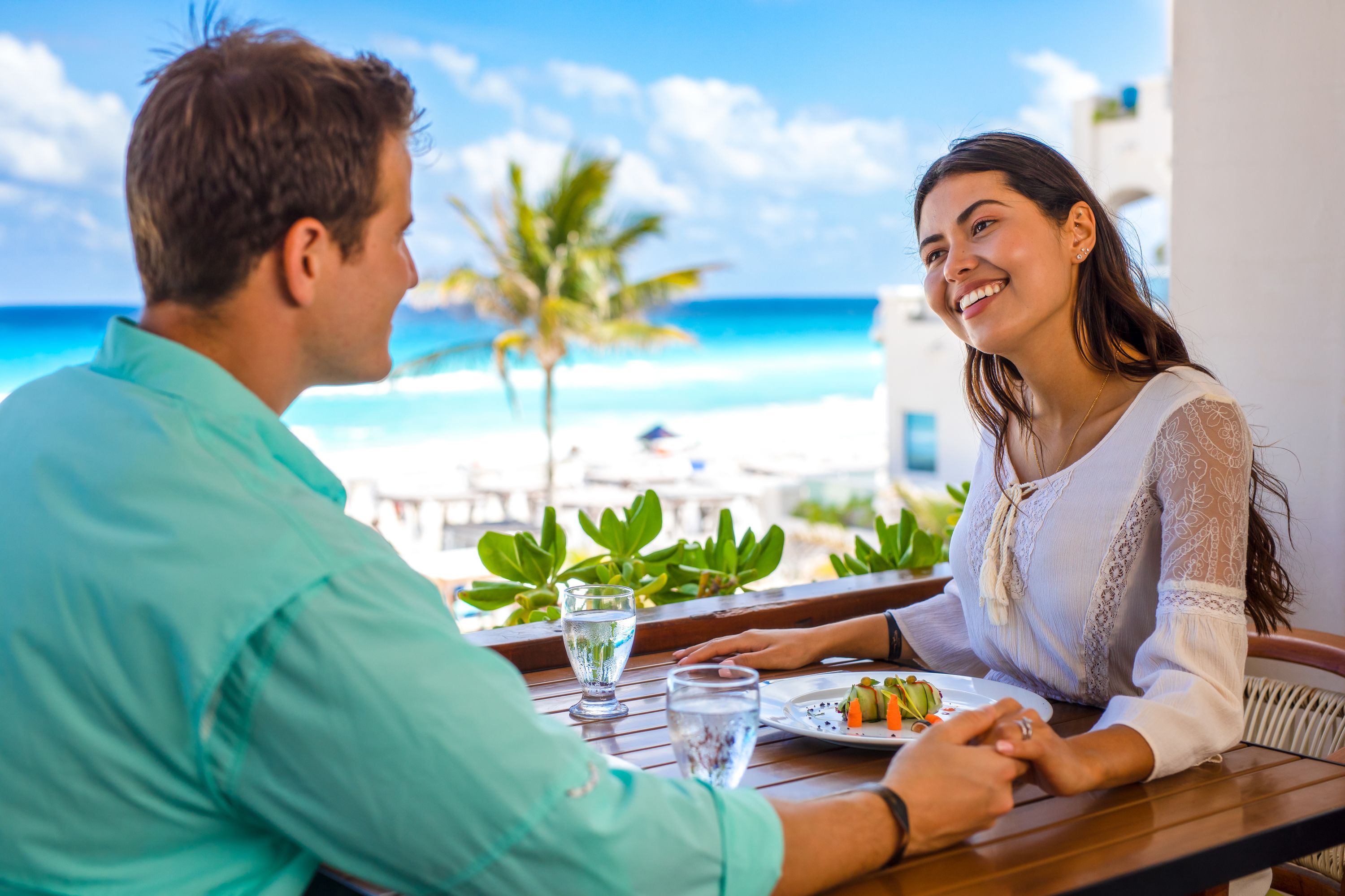 A couple dining at a table with a view of the beach and palm trees.