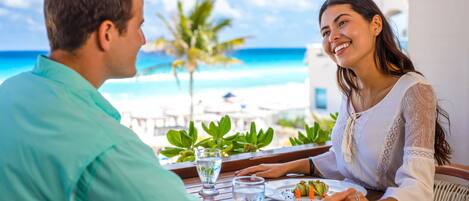 A couple dining at a table with a view of the beach and palm trees.