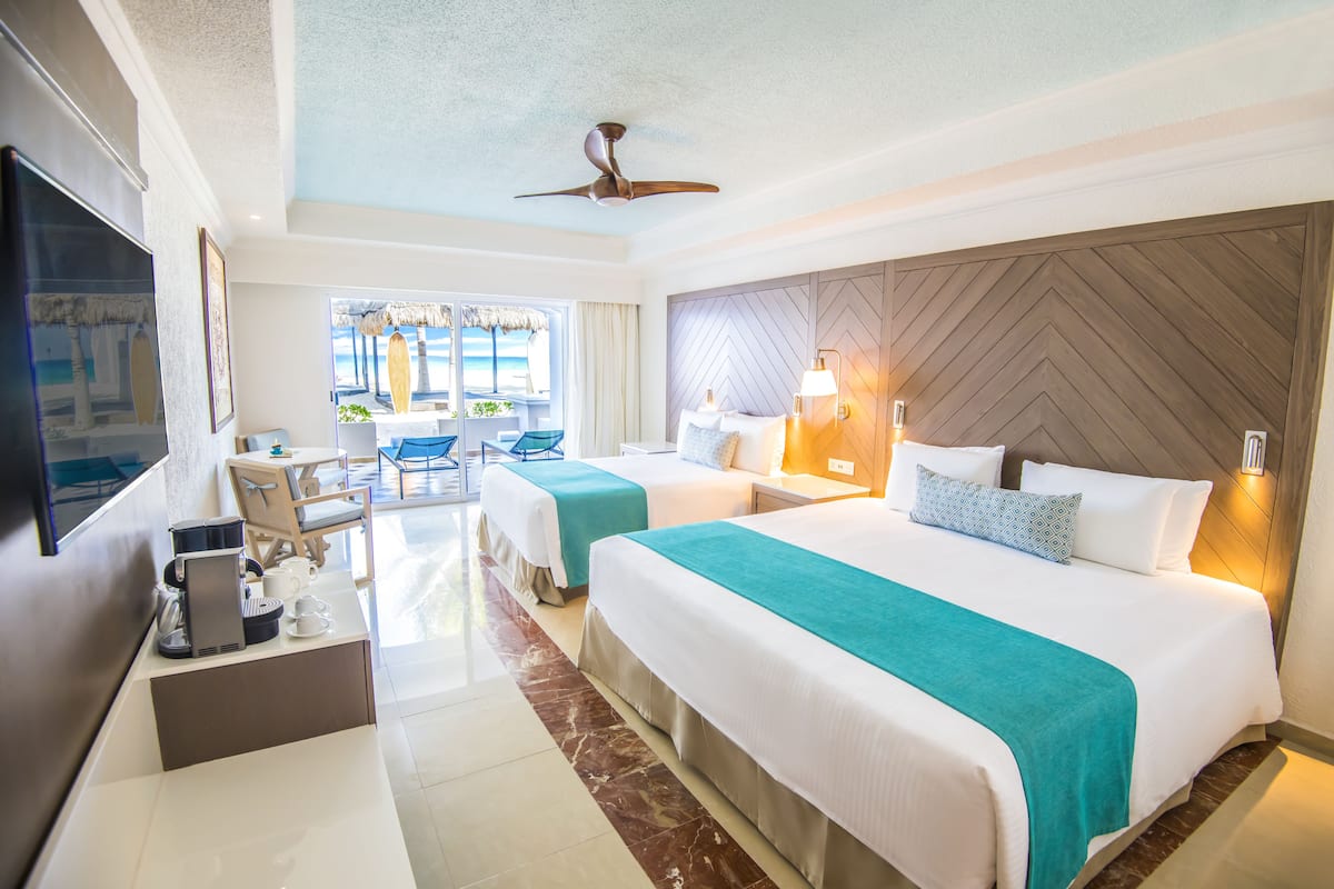 A hotel room with two beds, a TV, a coffee maker, and a view of the beach.