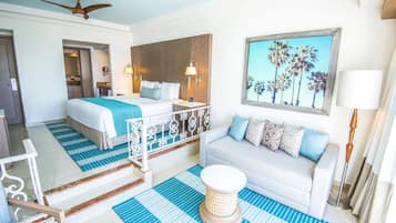 A hotel room with a bed, a sofa, a painting of palm trees, a ceiling fan, and a window with curtains.