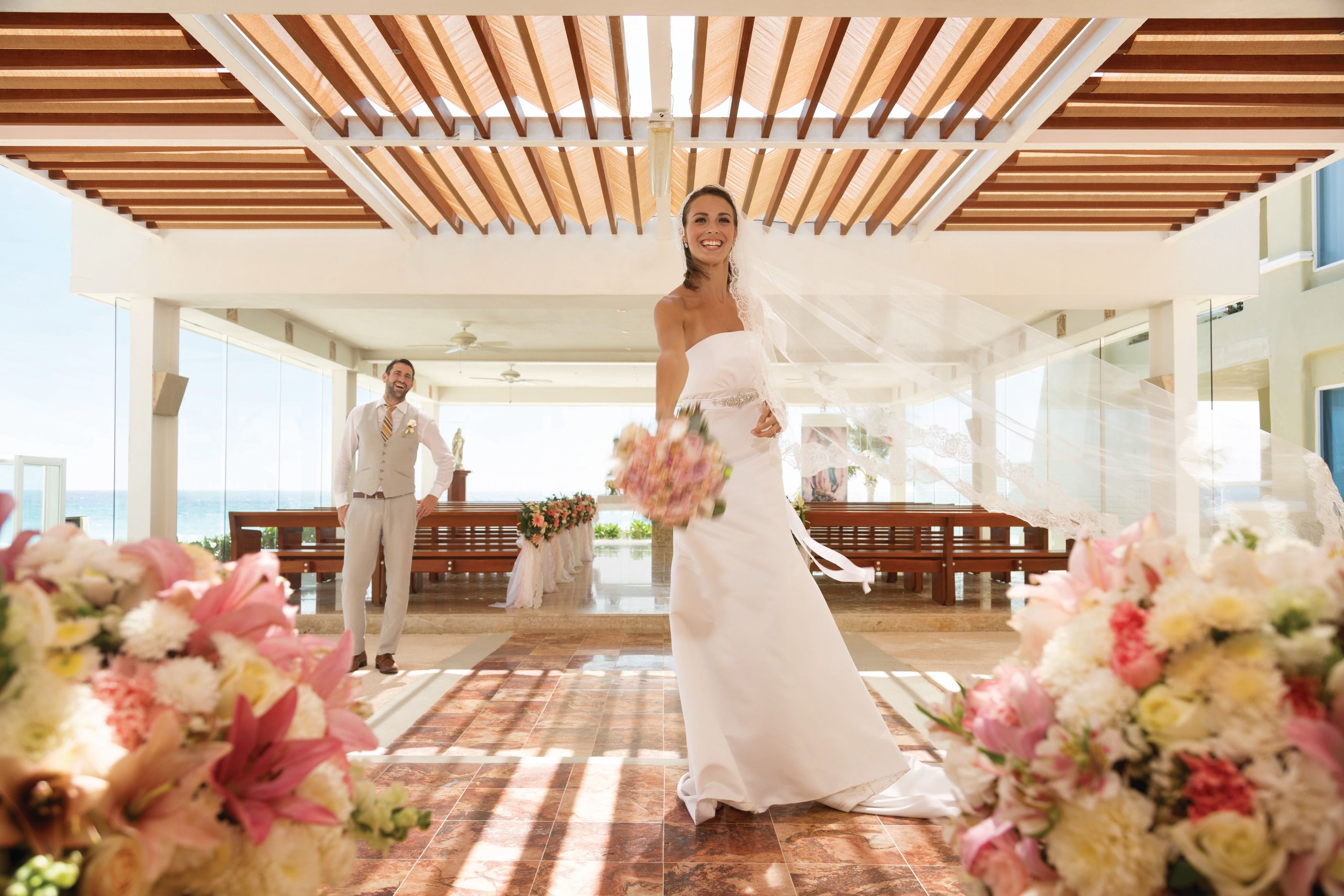 Uma cerimônia de casamento em um salão amplo com teto de madeira e grandes janelas com vista para um corpo d'água.