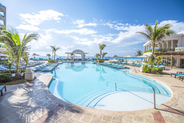 Relax by the pool overlooking the ocean, surrounded by palm trees and lounge chairs.