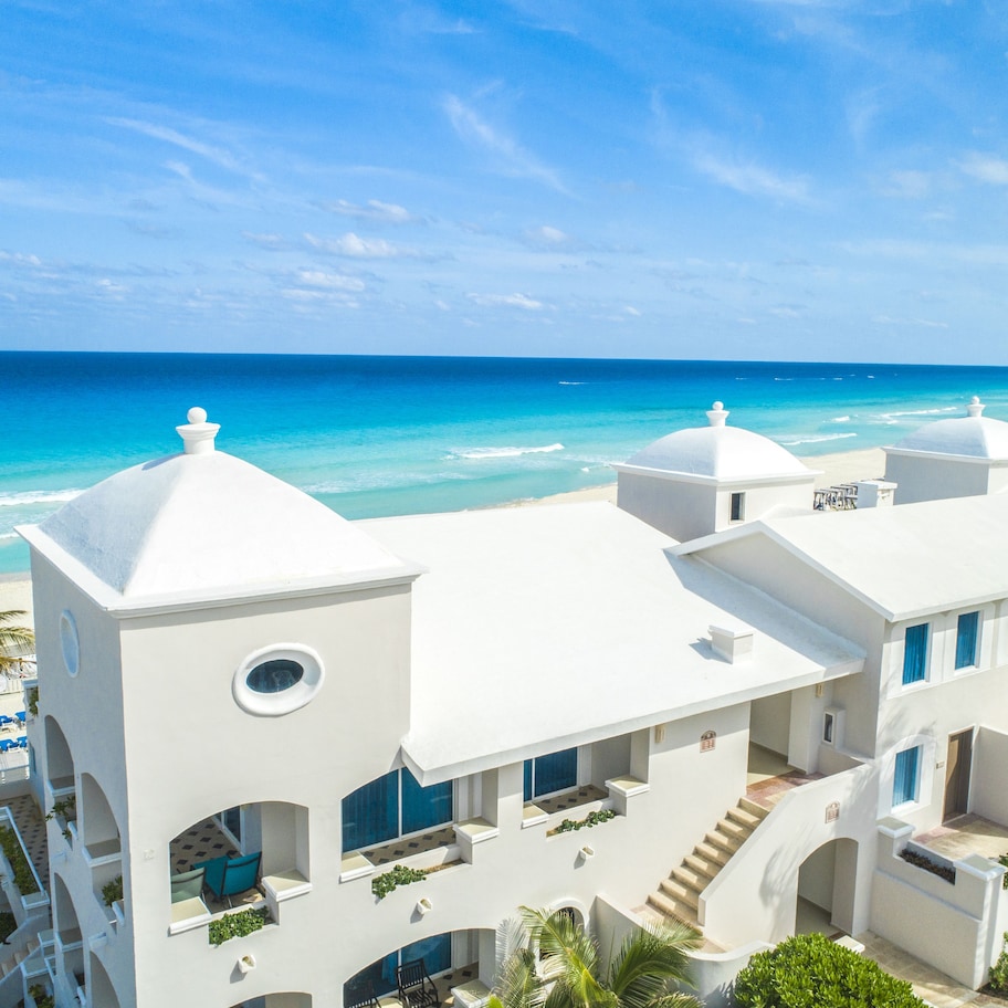 A white building with a beach view, multiple balconies, and a pool area.