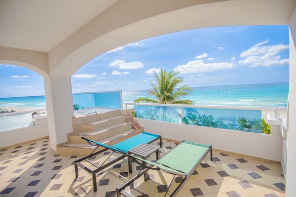A balcony with a view of the ocean, a palm tree, and a tiled floor.