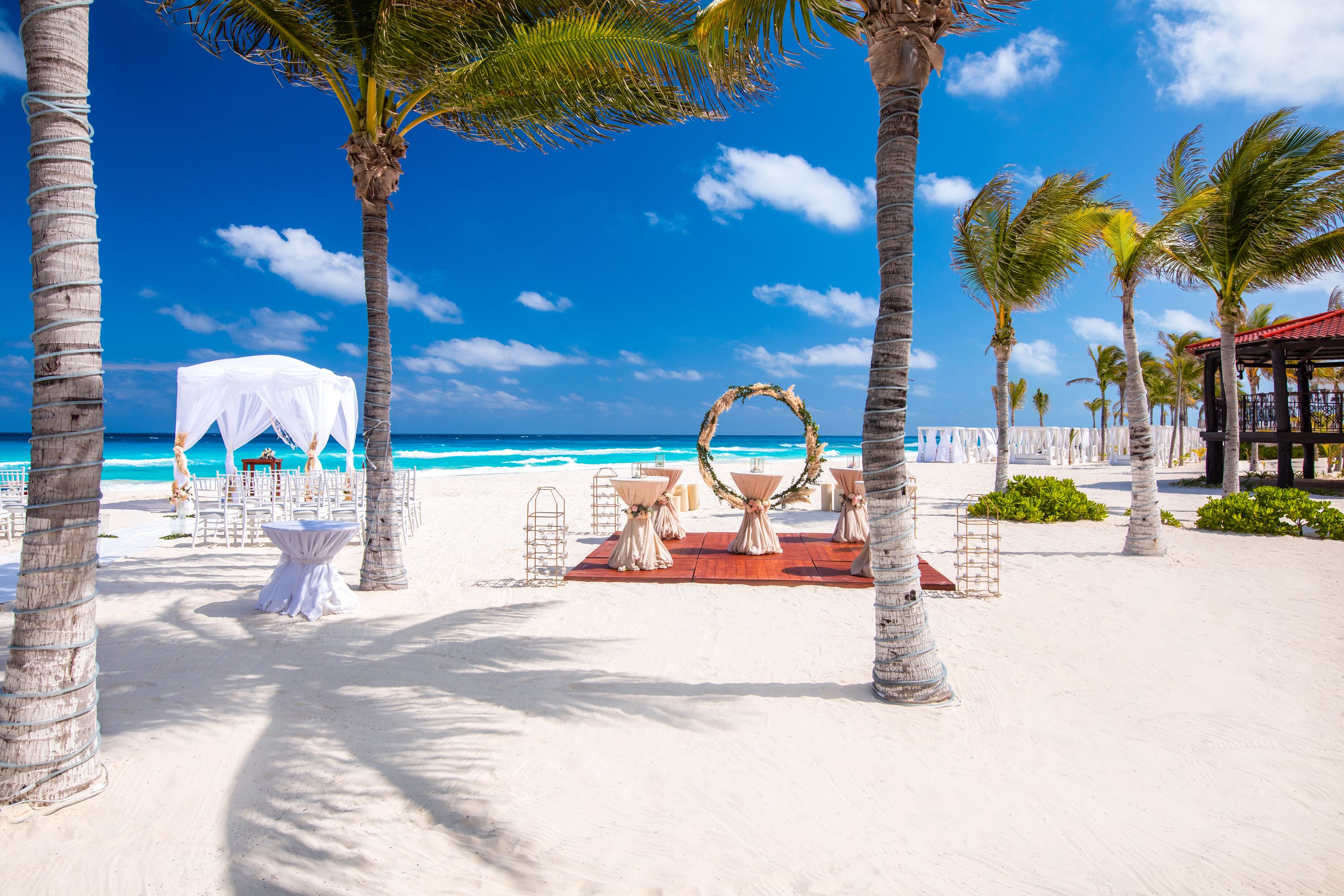 A beach wedding setup with a white canopy, tables with white tablecloths, and a decorative arch.
