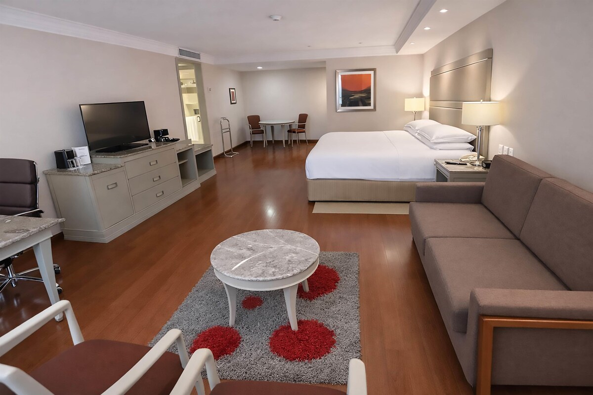 A hotel room with a bed, a sofa, a TV, a desk, and a chair.
