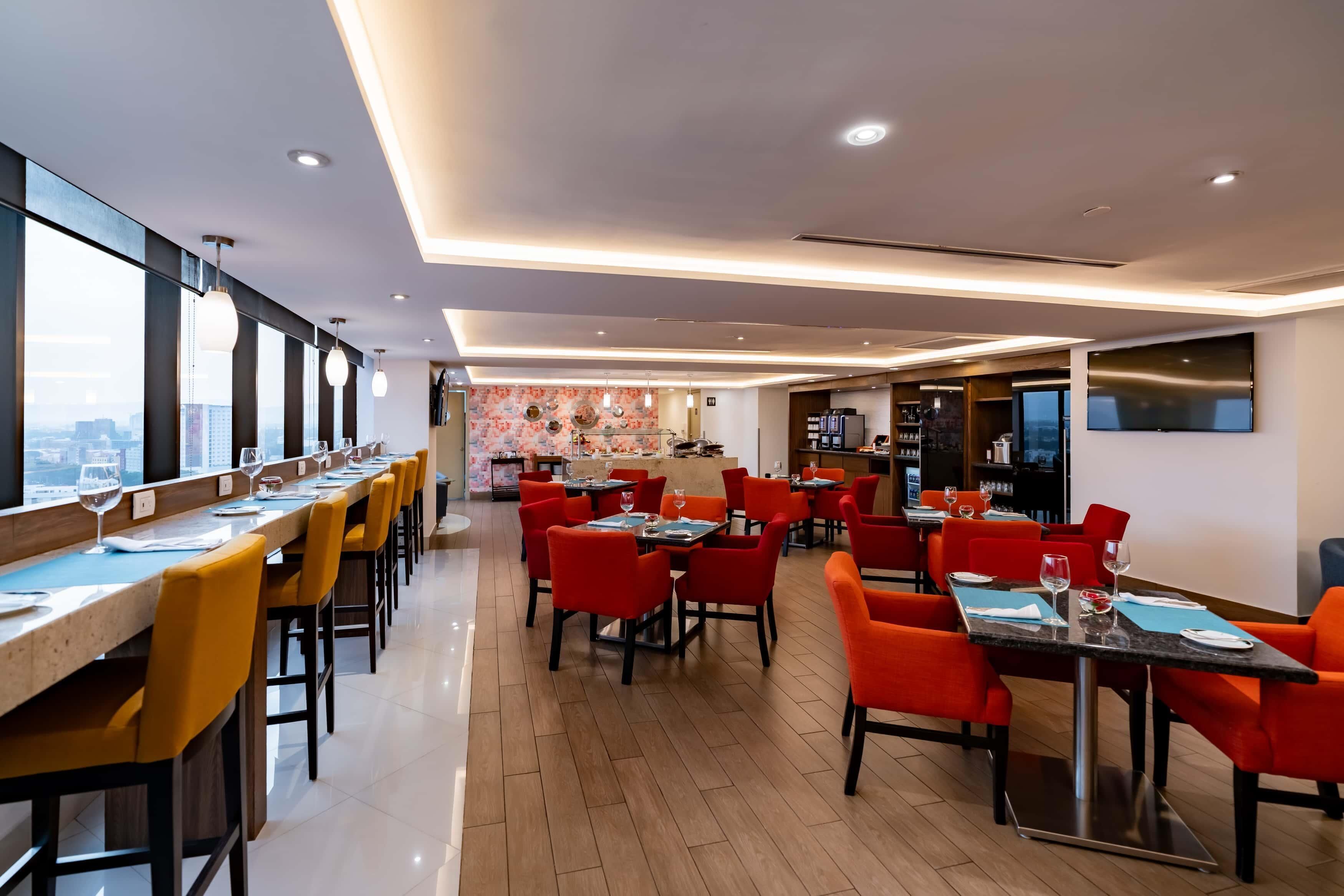 A modern dining area with high tables and chairs, a kitchen area, and a city view.