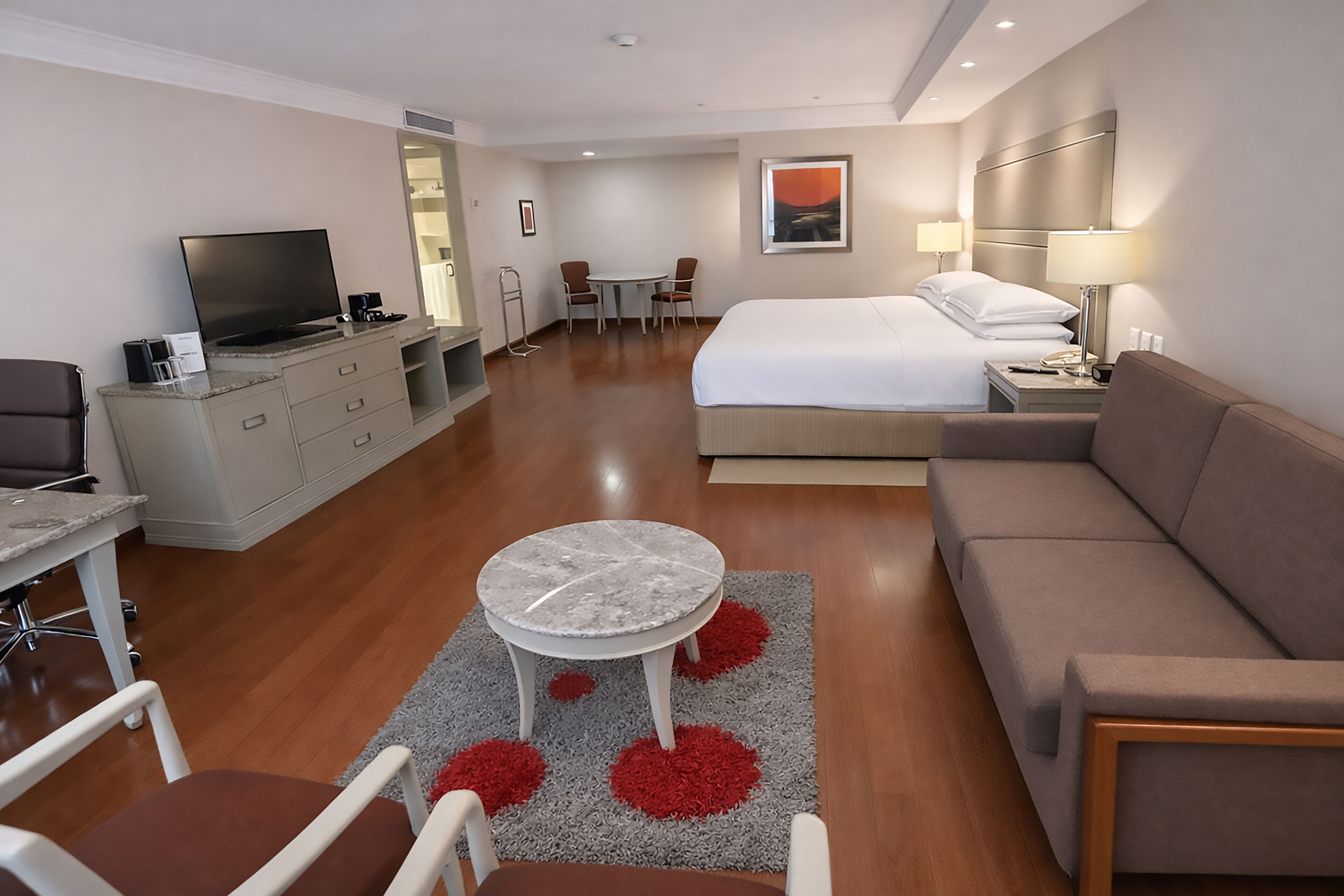 A hotel room with a bed, a sofa, a TV, a desk, and a dining area.
