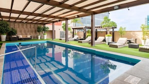 Un área de piscina exterior moderna con una pérgola, sillas de descanso y vistas a la ciudad.