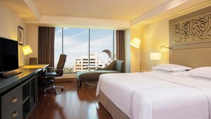 Habitación de hotel con cama, escritorio, silla y un ventanal con vistas a la ciudad.