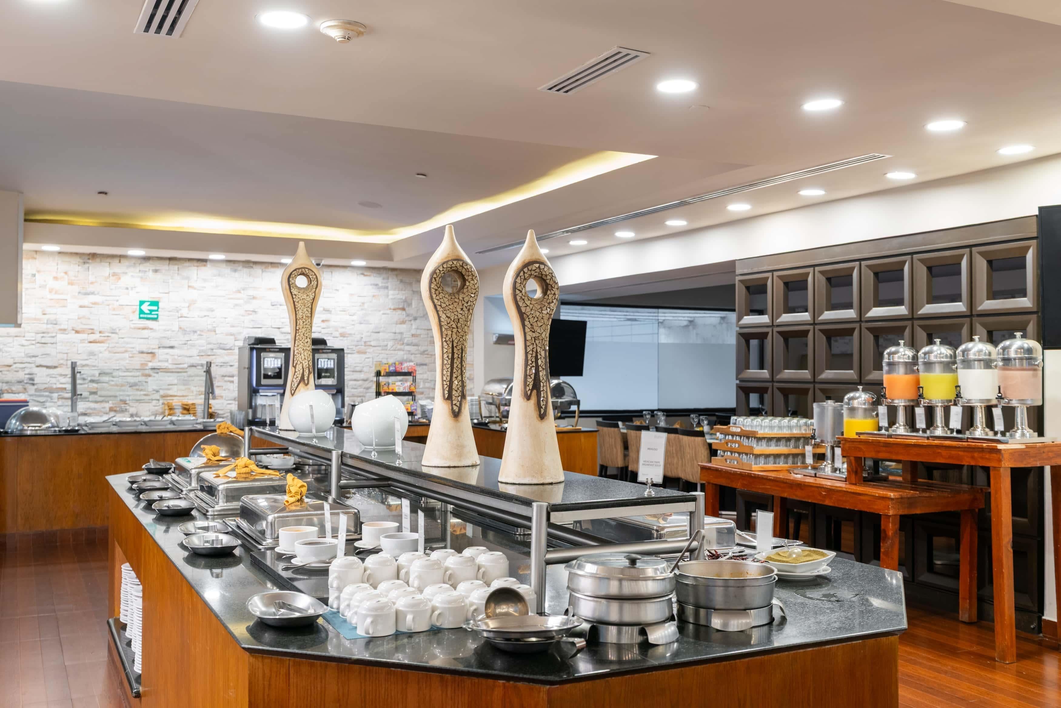 Zona de bufé con diversos platos, utensilios de servicio y jarrones decorativos.