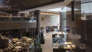 Un moderno hall de hotel con varias zonas de estar, un restaurante visible y un amplio ventanal que ofrece vistas del interior.