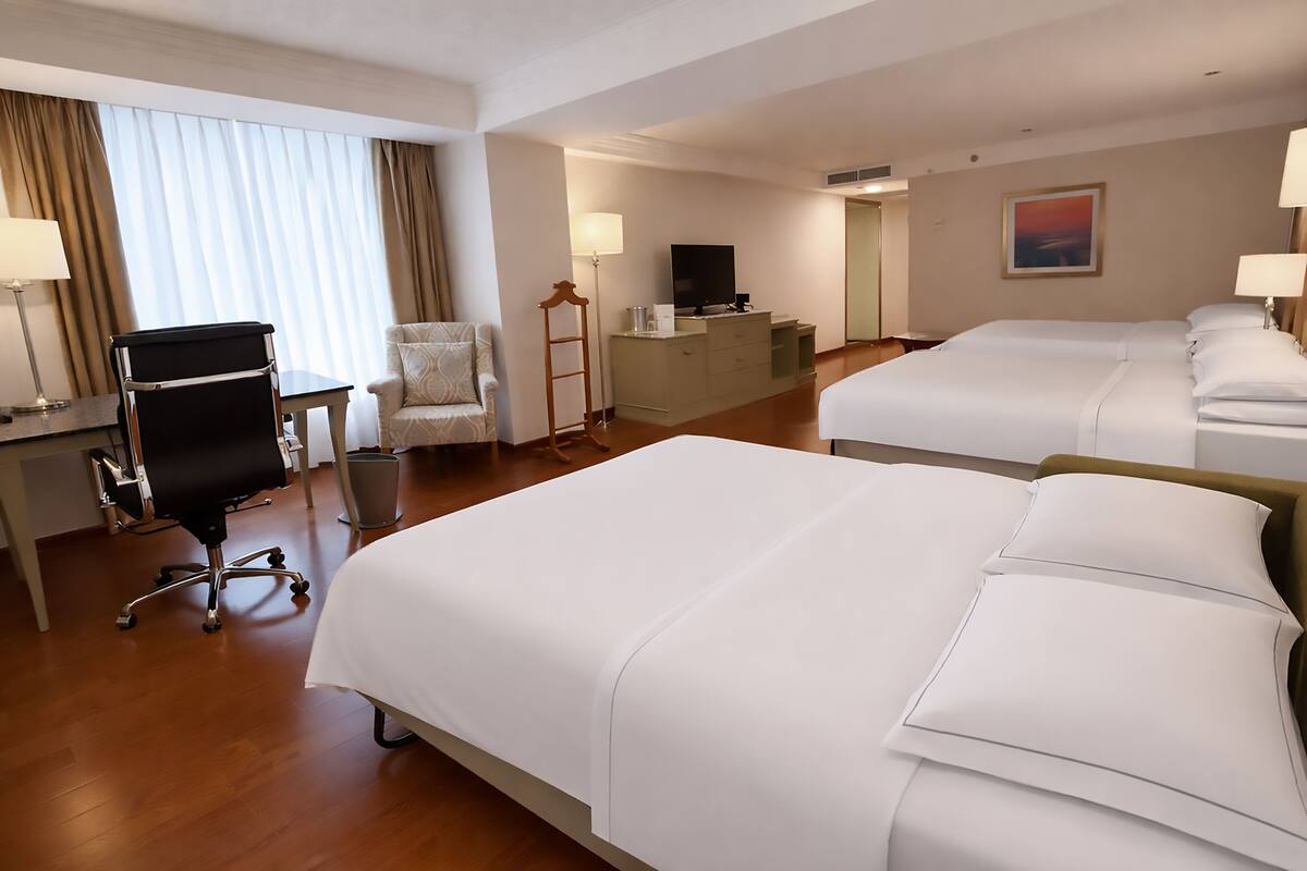 A hotel room with two beds, a desk, a chair, a television, and a painting on the wall.