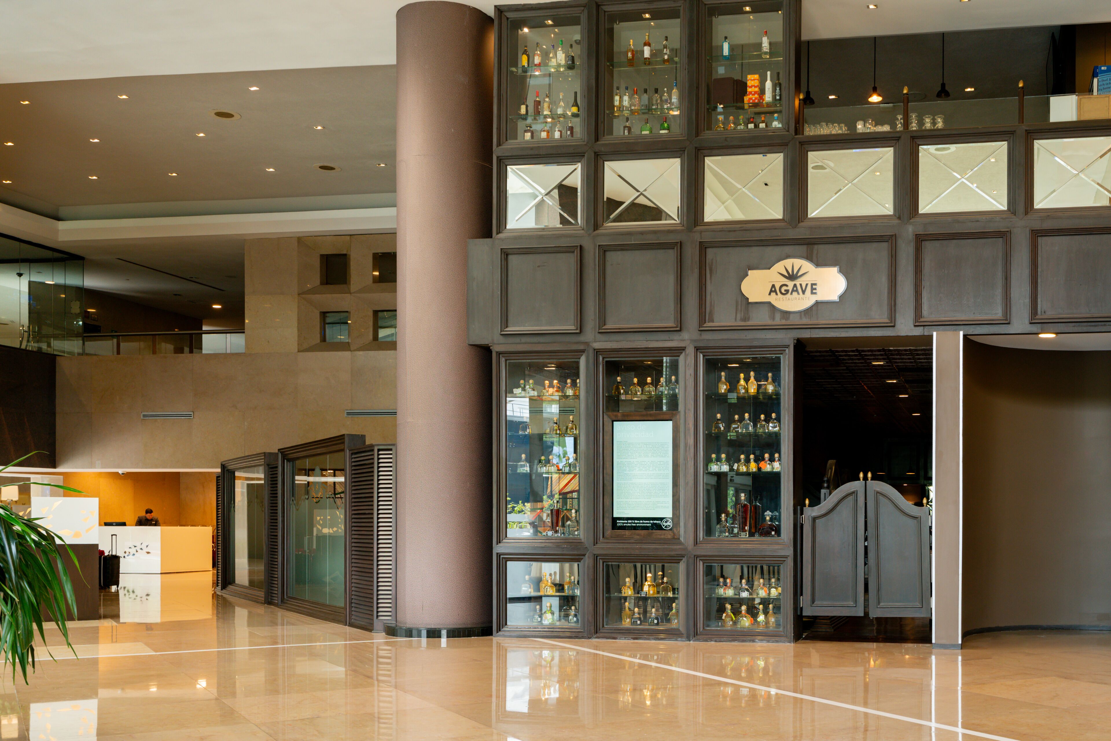Un moderno vestíbulo de hotel con una zona de bar con ventanales, un mostrador de recepción y un pilar grande.