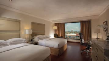 Quarto de hotel com duas camas, uma mesa, uma cadeira e vista para a cidade.