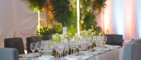 A long dining table set with multiple wine glasses, plates, and a centerpiece of flowers.