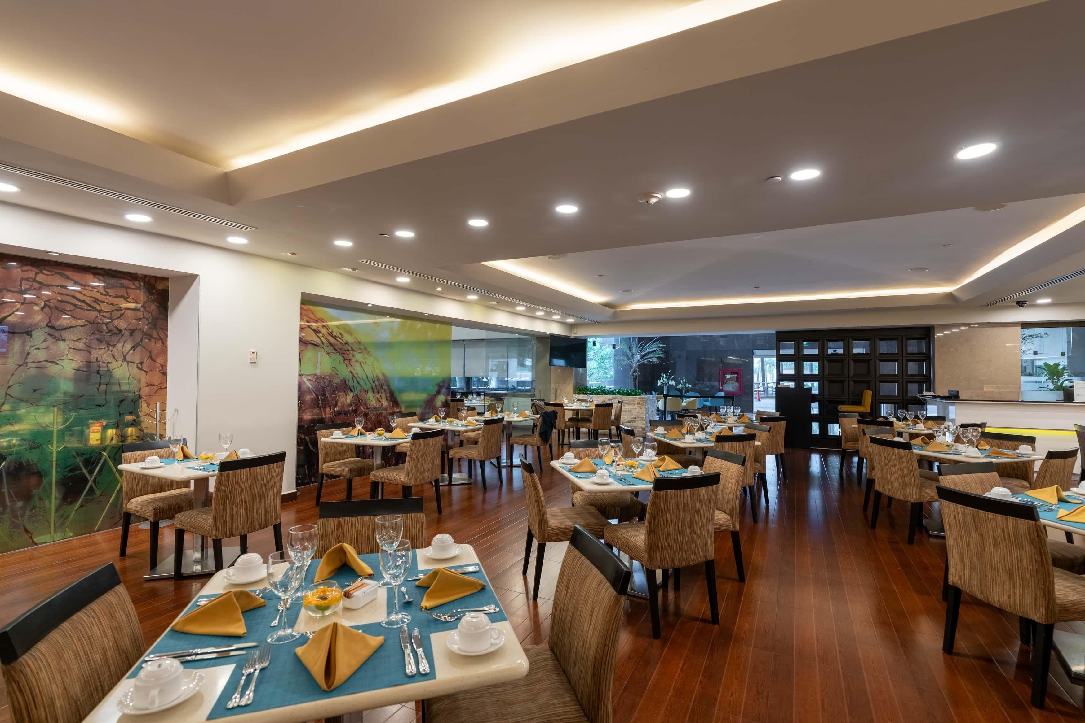 A spacious restaurant with multiple dining tables, chairs, and a modern ceiling design.