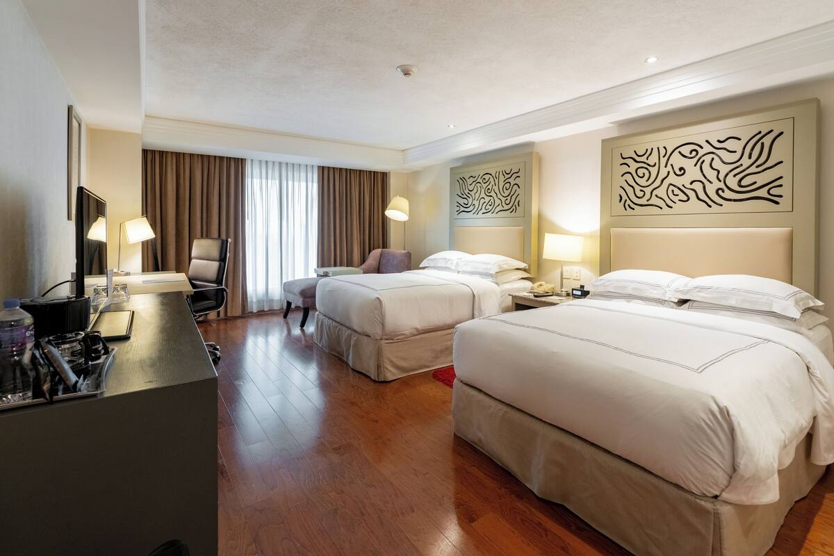 A hotel room with two beds, a desk with a telephone, a chair, and a desk lamp.