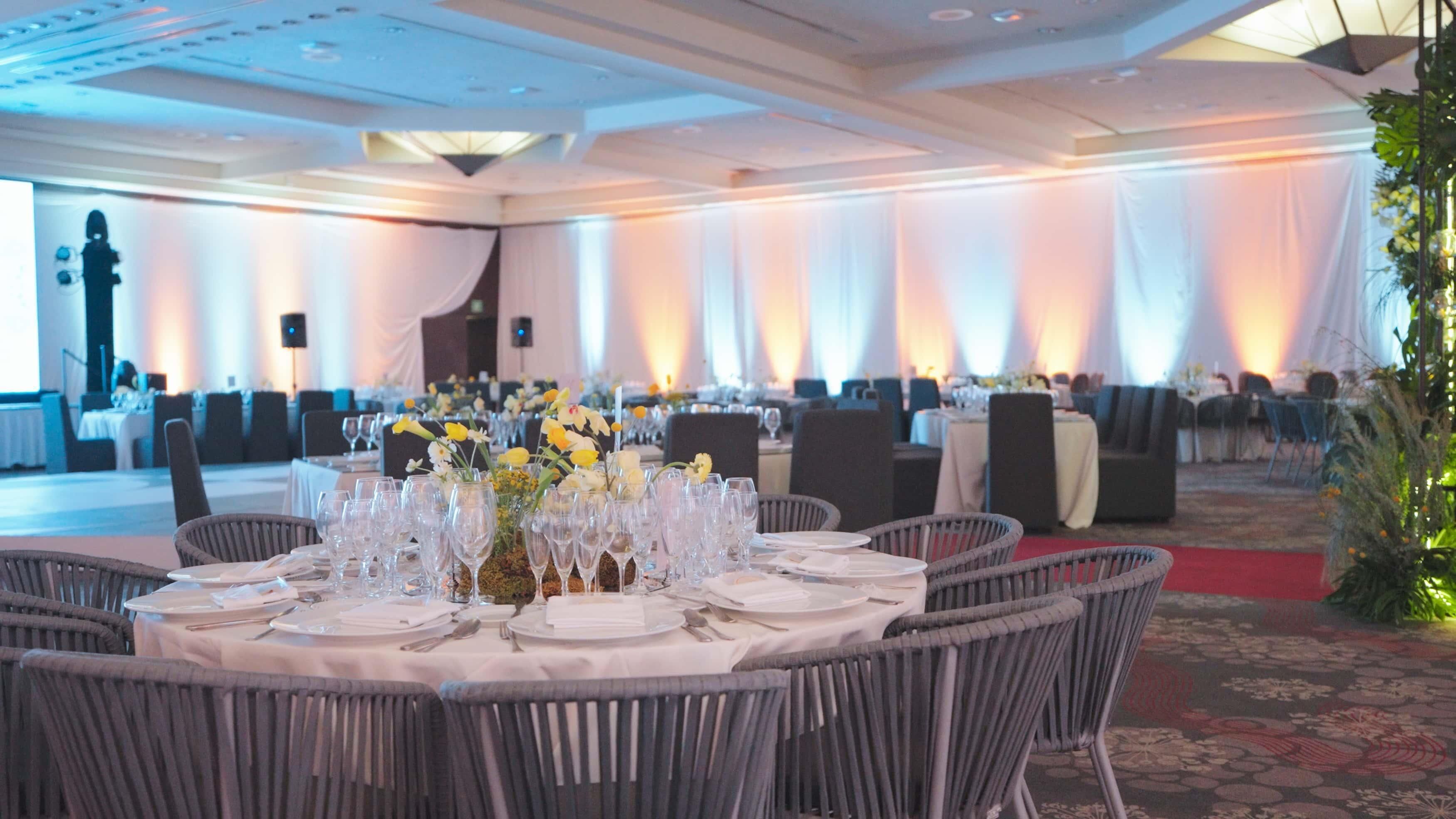 Une salle de banquet avec des tables rondes dressées pour un événement formel, agrémentée de nappes blanches et de compositions florales.