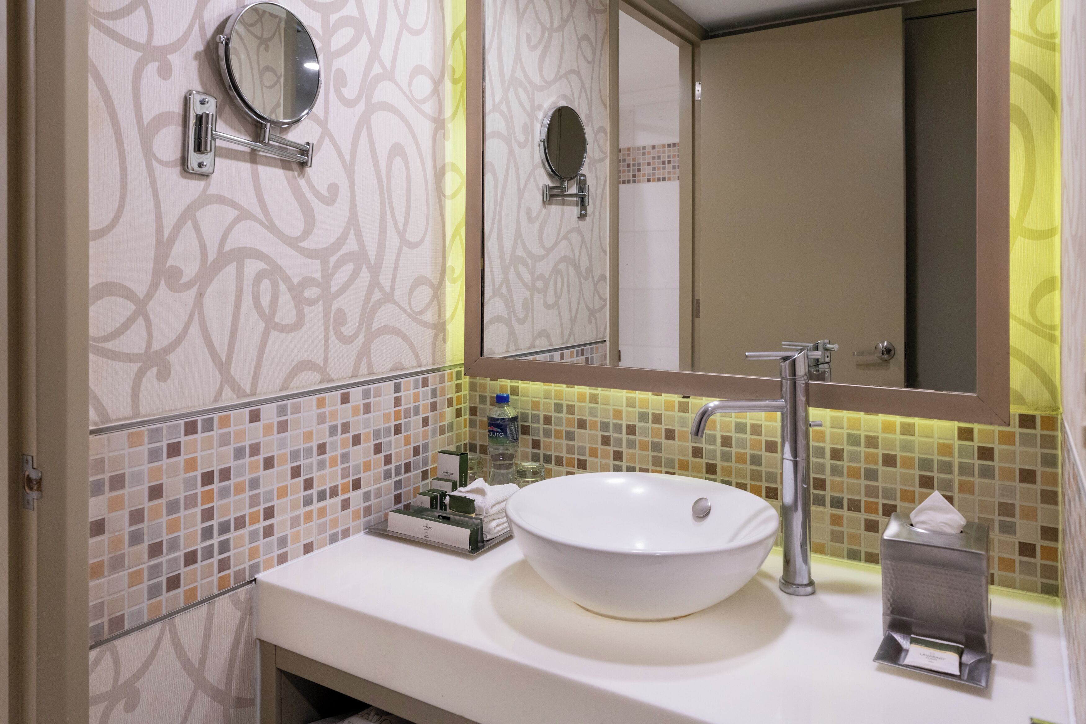 Un baño con lavamanos blanco, un espejo, dispensador de toallas y una botella de jabón para manos.
