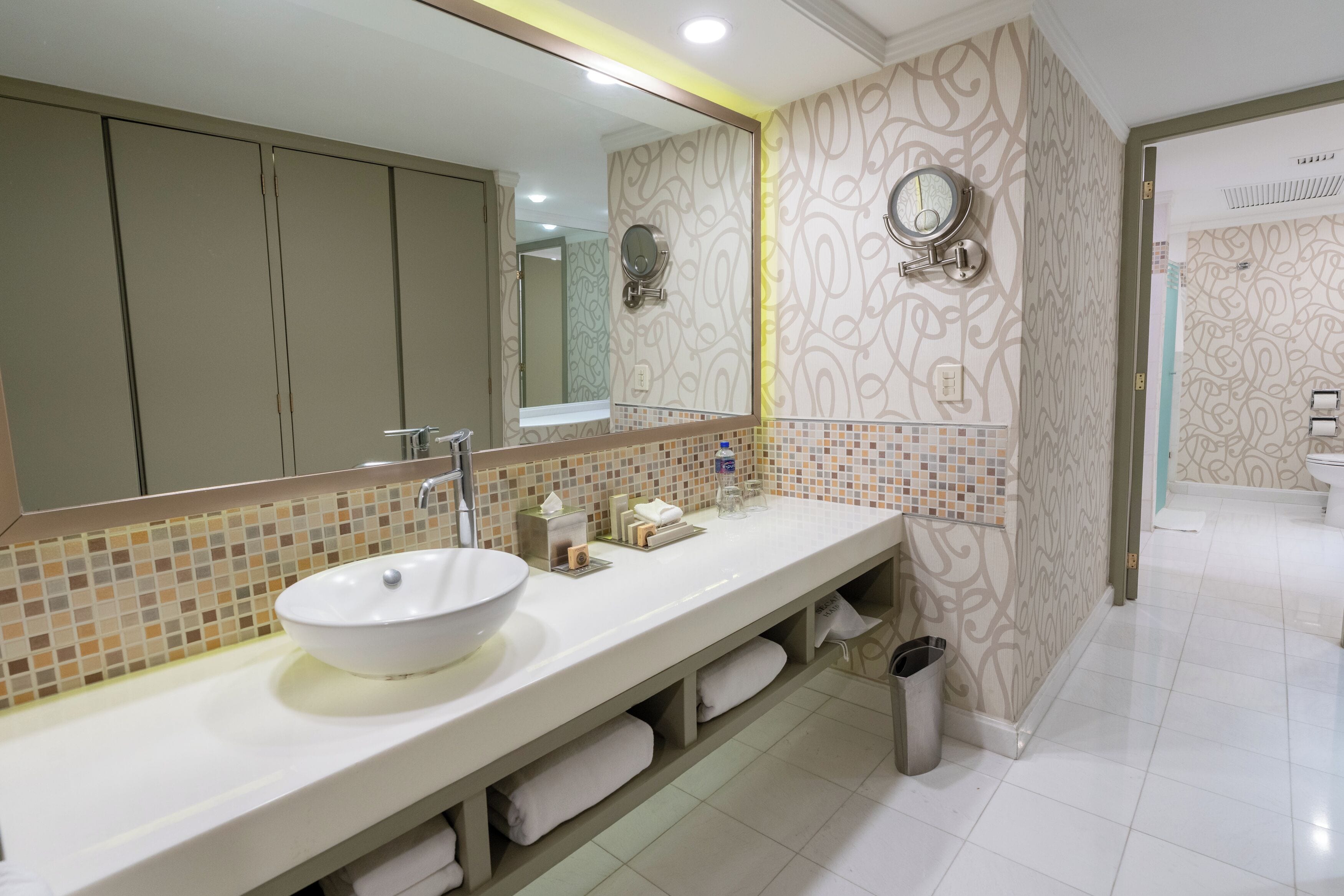 A modern bathroom with a large mirror, a white sink, and a towel rack.
