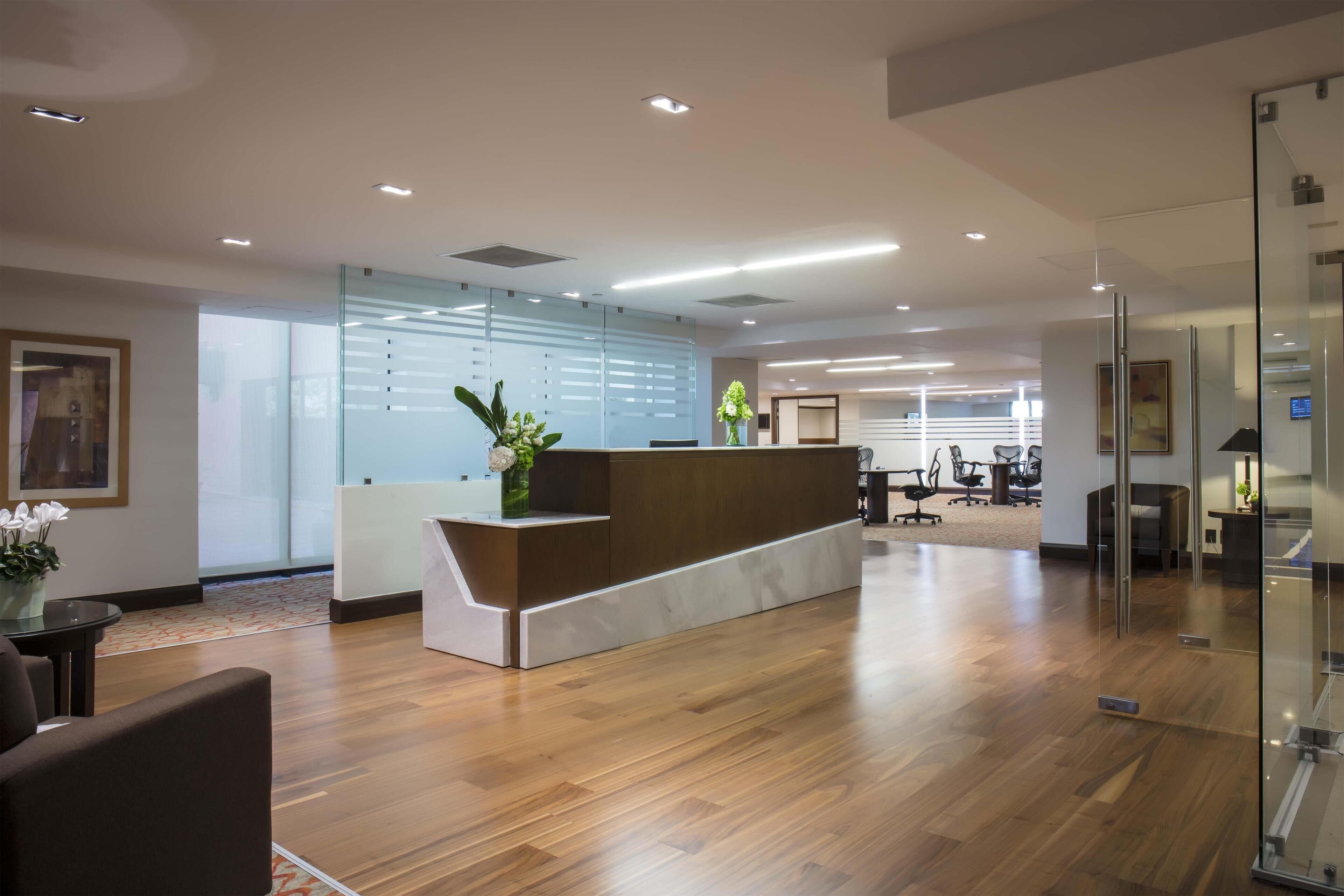 A modern reception area with a wooden reception desk, glass partitions, and a seating area with chairs.