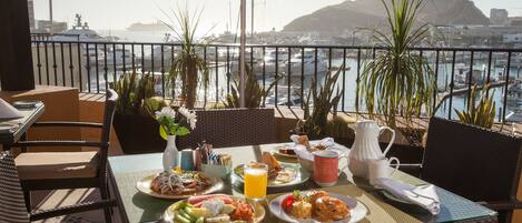 Una tavola imbandita con prodotti per la colazione e vista su barche e una montagna.
