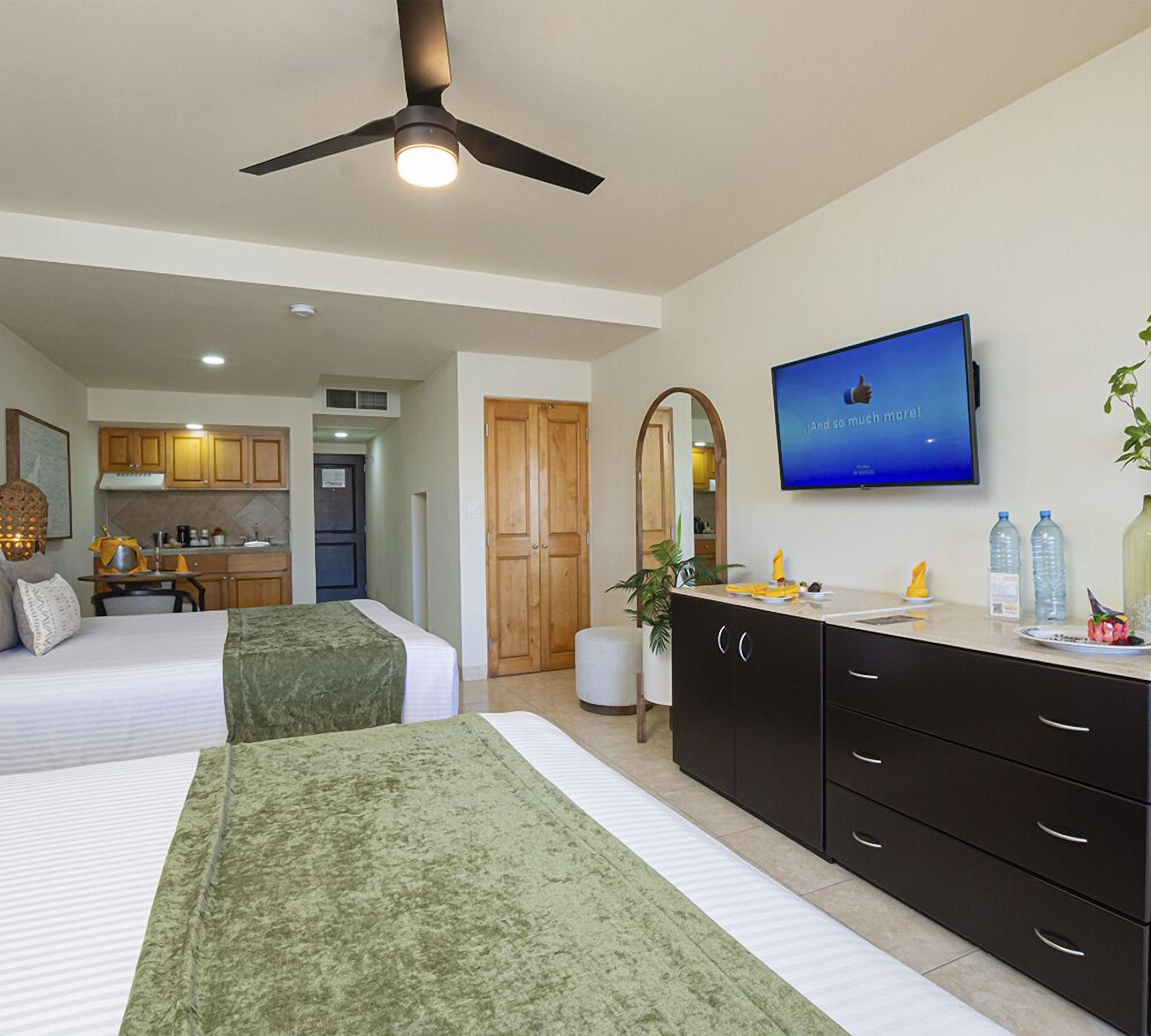 Habitación de hotel con dos camas, televisión, kitchenette y espejo.