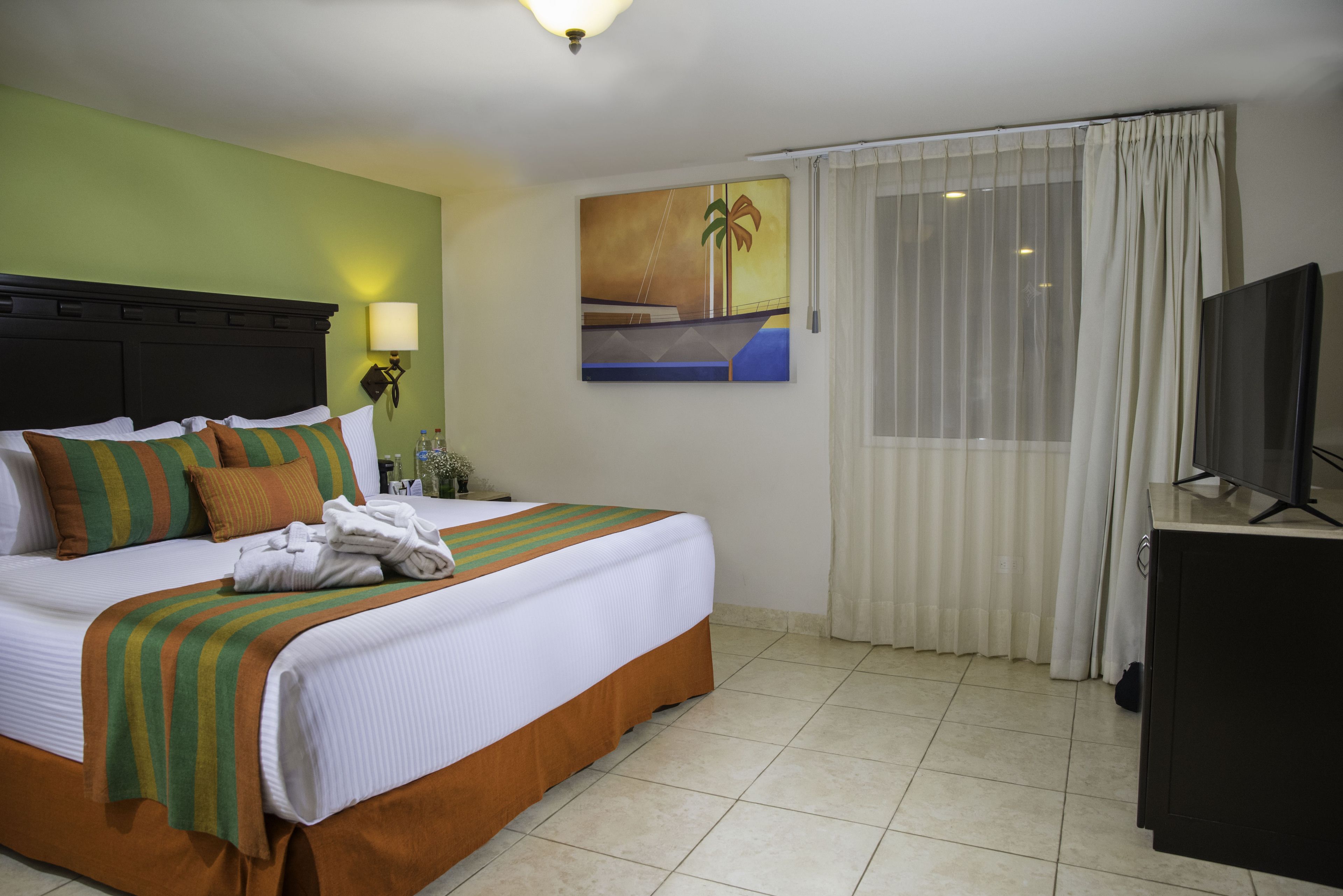 Een hotelkamer met een bed, een televisie, een schilderij en een raam met gordijnen.