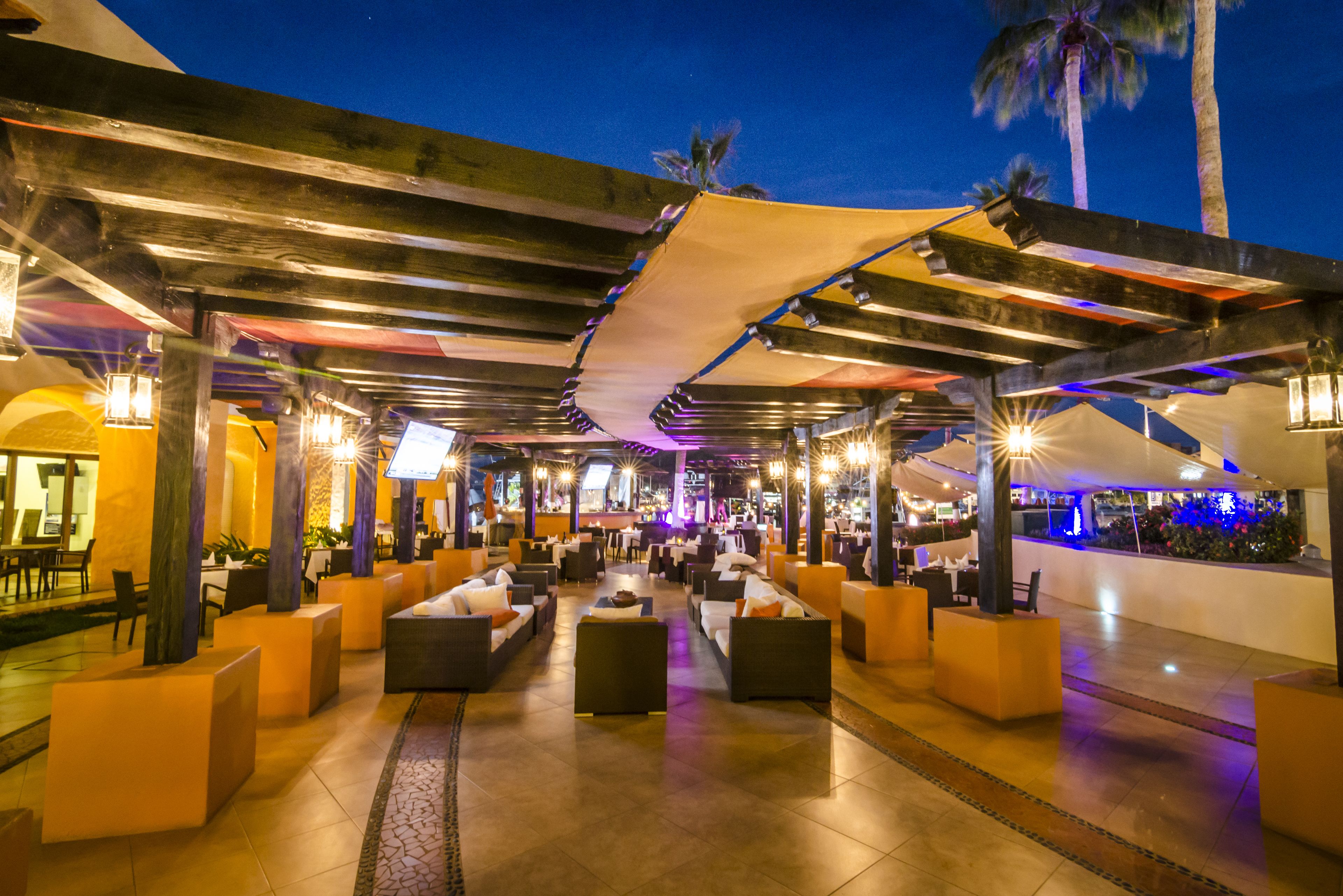 Un área de lounge al aire libre con disposición de asientos y un bar al fondo.