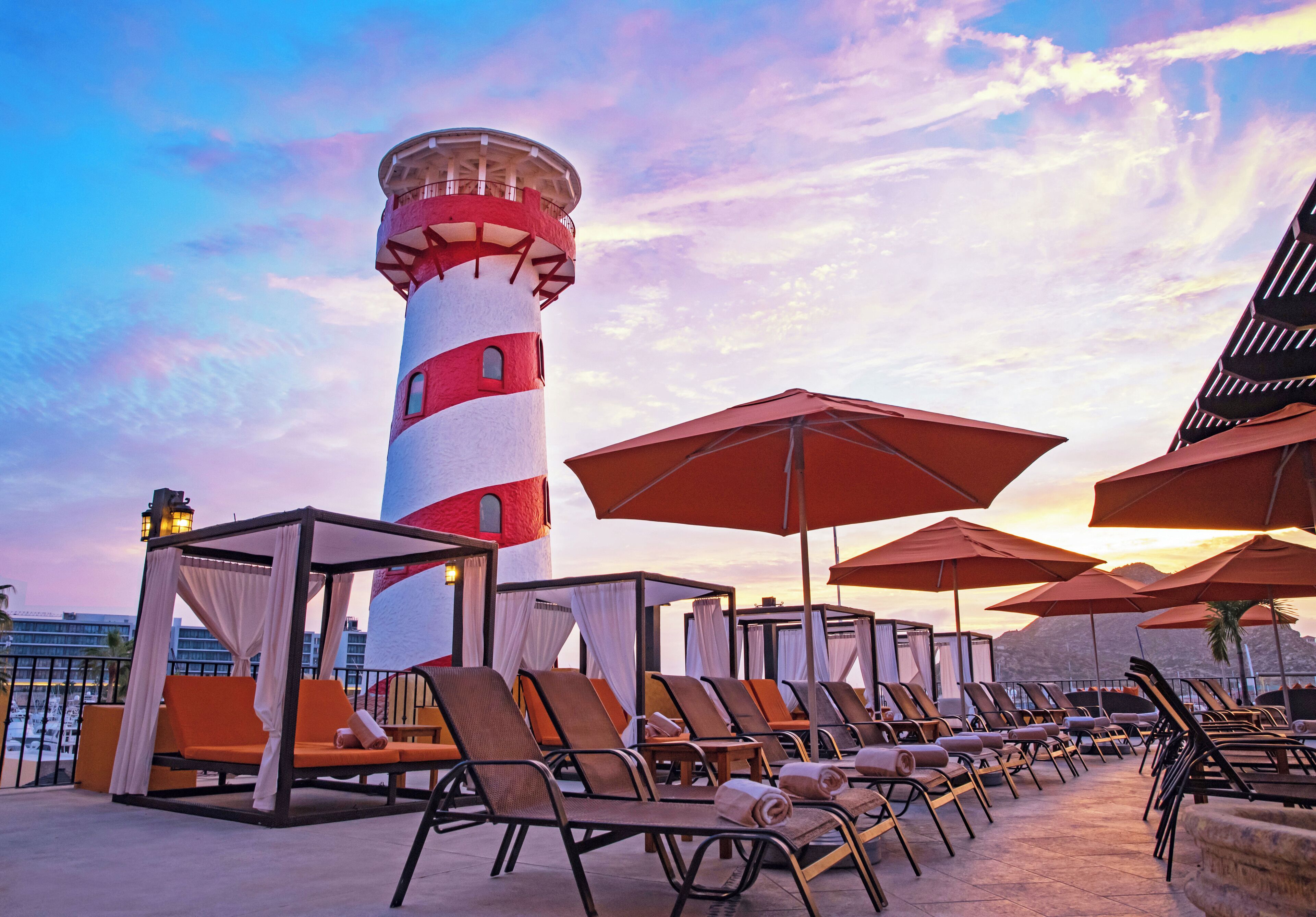 Un espace de détente sur le toit, avec des fauteuils et des parasols, un phare rouge et blanc, et une vue sur l’océan.