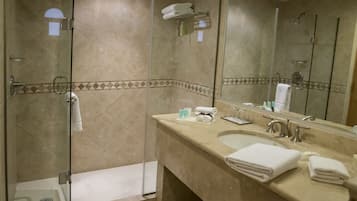 A modern bathroom with a glass-enclosed shower, a large mirror, and a beige countertop with toiletries.